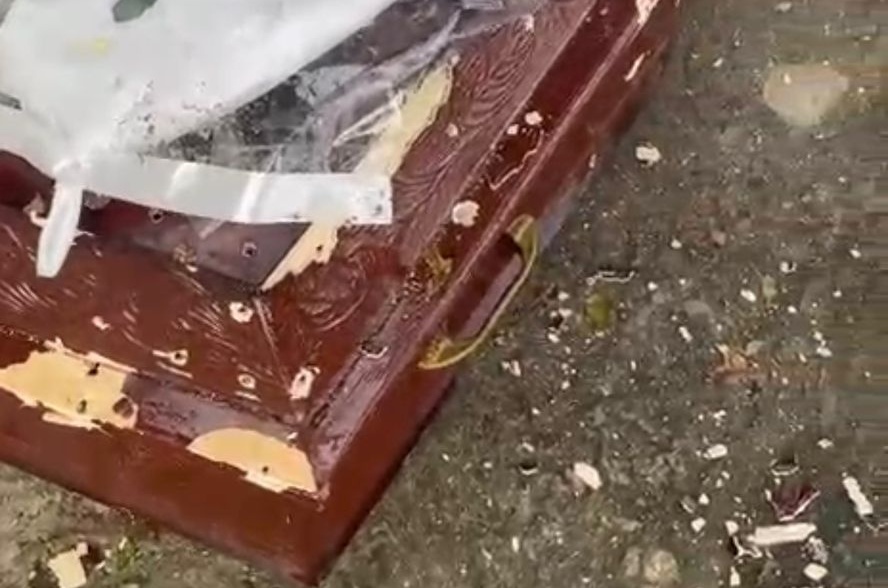 Homens metralham caixão com defunto dentro.