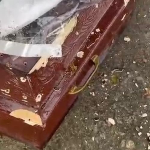 Homens metralham caixão com defunto dentro.
